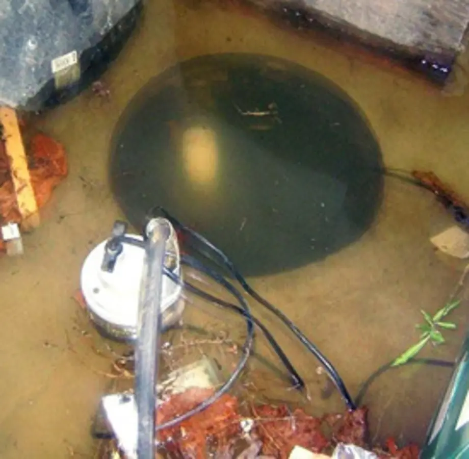 Sump pump submerged in murky water with debris and cables inside a flooded area.