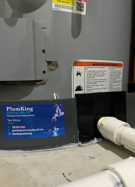 Zoomed-in photo of the RetroSeal device connected to a drainage output with PlumKing Contracting's business card clearly displayed on the outer wall of the device.