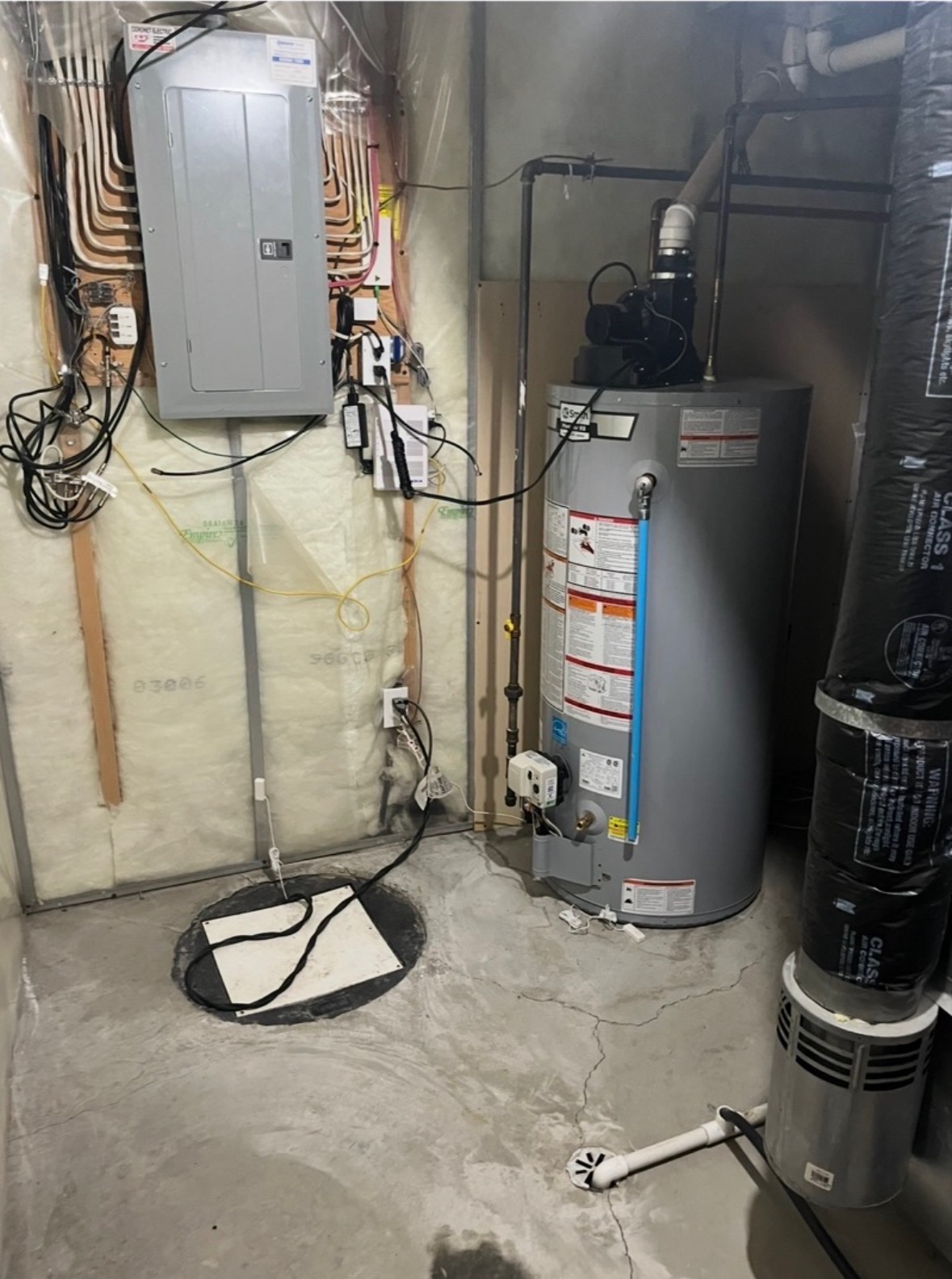 Basement utility room with a water heater, electrical panel, sump pump pit, and ductwork pipes.