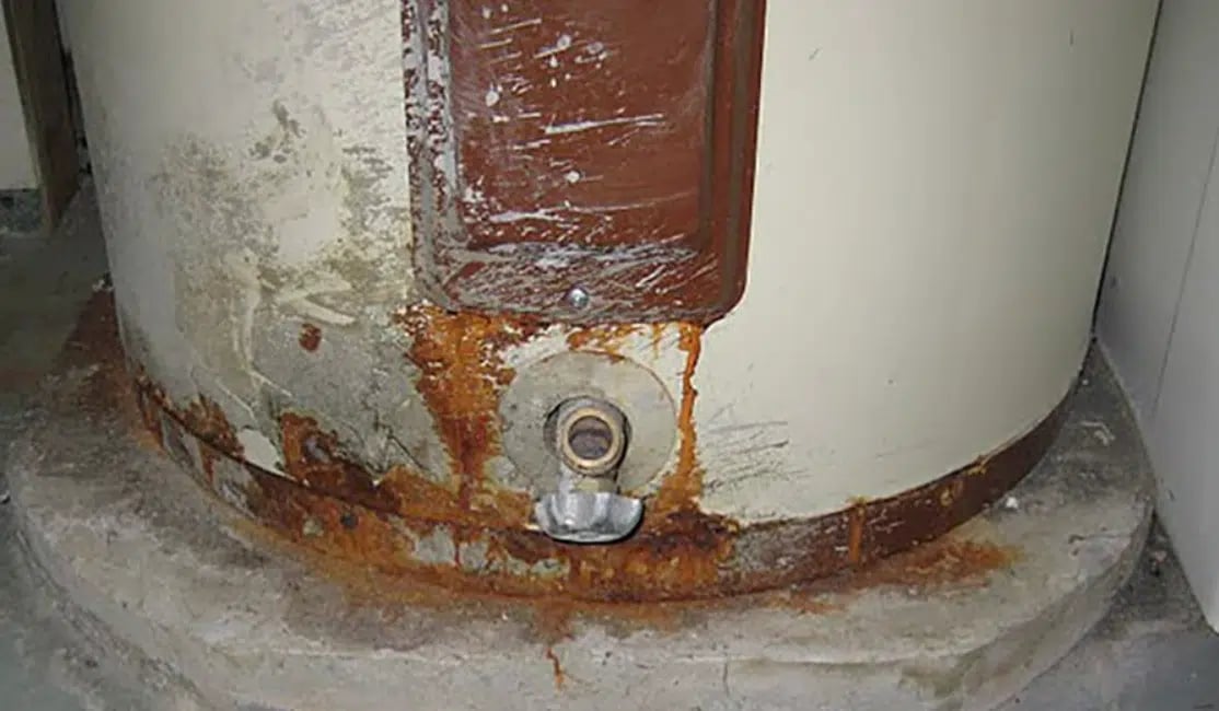 Rusty and corroded bottom part of a water heater tank on a concrete base.