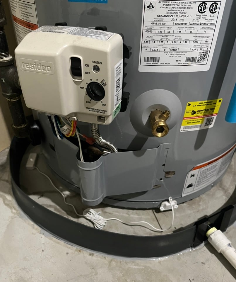 Close-up of a gas water heater control panel with status switch, dial, and labels on grey tank.