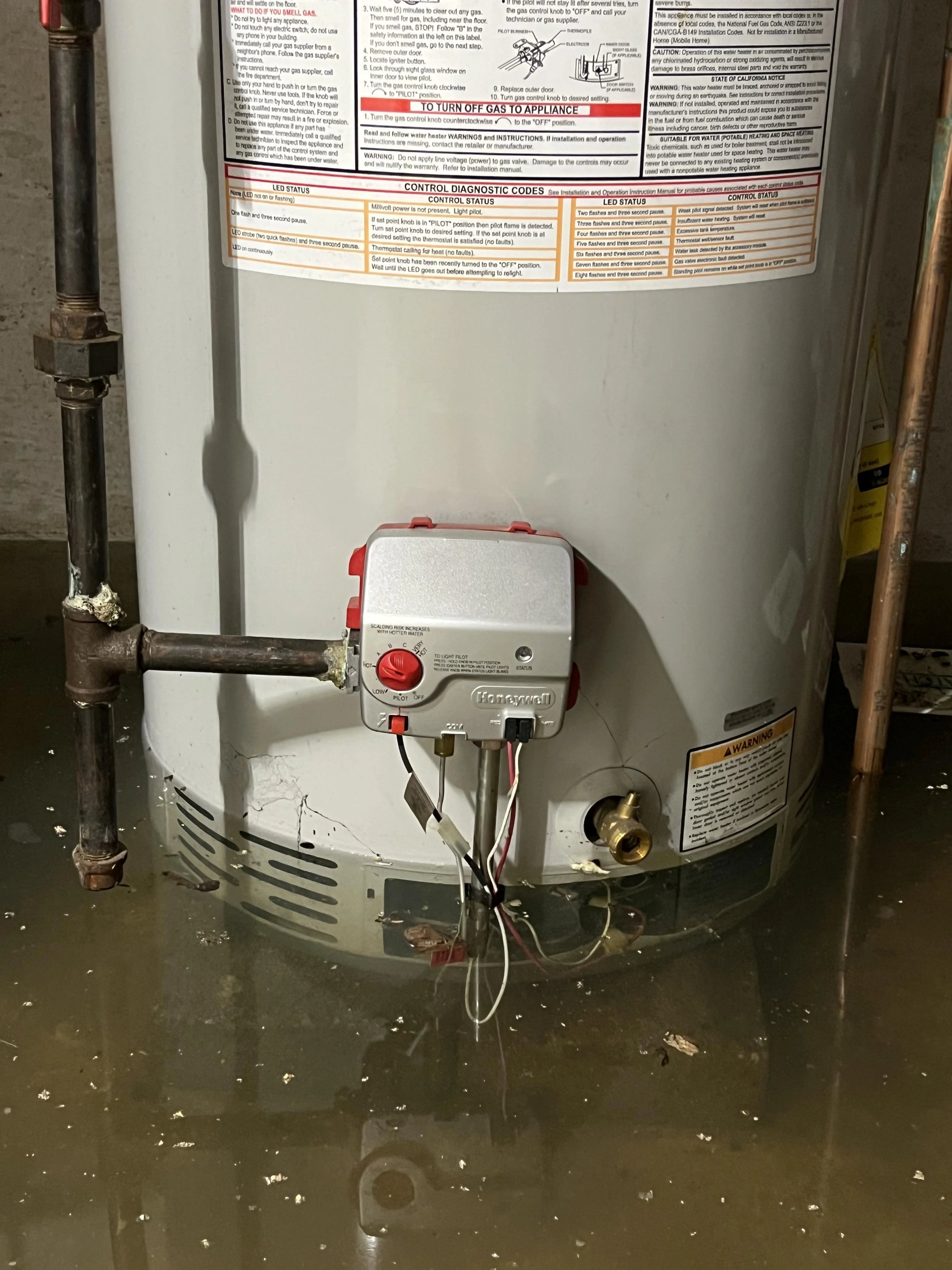 Bottom section of a water heater partially submerged in standing water in a basement.
