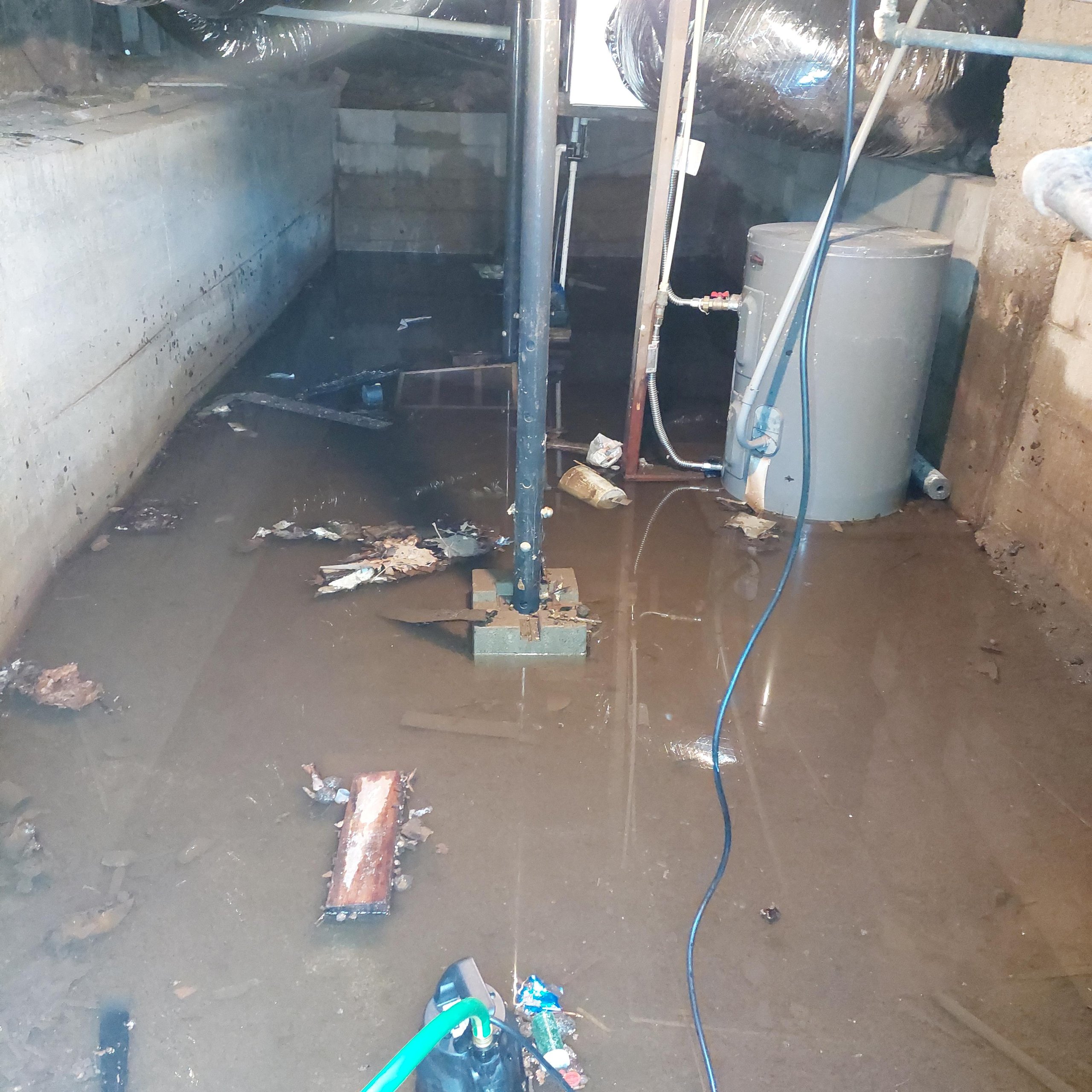 Basement partially flooded with murky water, debris floating, and a water heater in the corner.