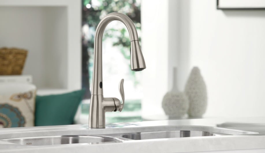 Modern stainless steel kitchen faucet with pull-down sprayer over double sink on marble countertop.