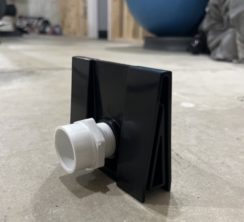 Black angled plastic stand with a white threaded pipe fitting attached on a concrete floor.